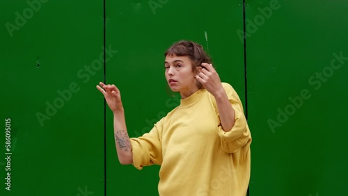hispanic young woman dancing in the street in yellow current clothes over green wall, latin girl practicing dance in motion with her hands
