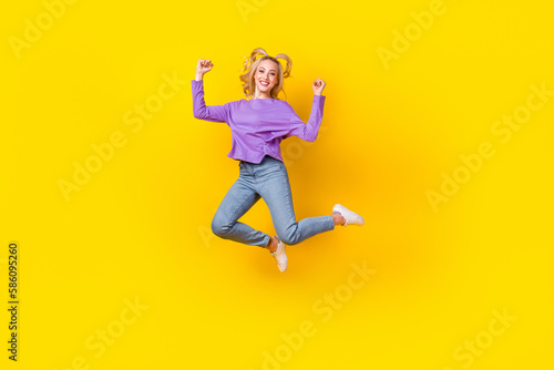 Full size photo of pretty young girl jumping raise fists have fun dressed stylish violet clothes isolated on yellow color background