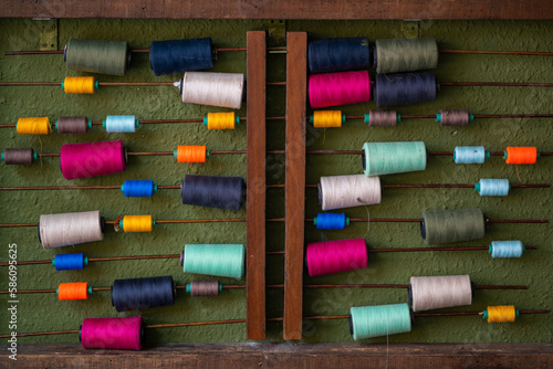 Colourful sewing threads hanging on old wooden sticks against a green texture wall. Decoration background. 