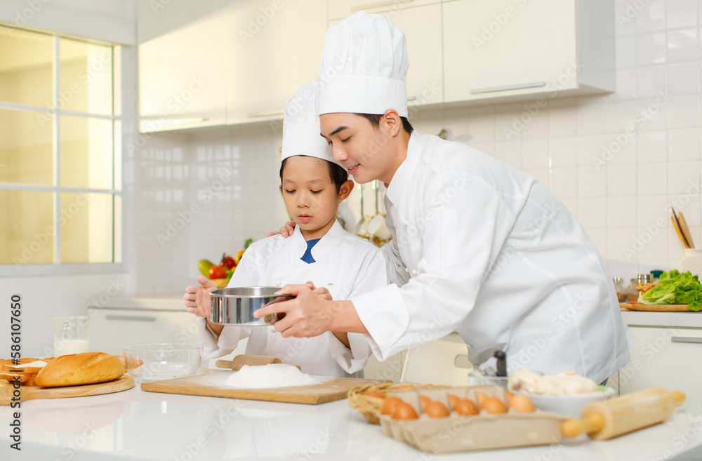 Asian young little boy pastry chef in white uniform with tall cook hat standing using stainless filter preparing sifting flour on wooden board while male cooking teacher helping teaching in kitchen Asian young little boy pastry chef in white uniform with tall cook hat standing using stainless filter preparing sifting flour on wooden board while male cooking teacher helping teaching in kitchen