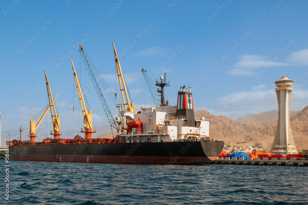 Jordan. Aqaba. Container ship moored at the dock for loading. There are several cranes on pier. Aqaba, Jordan, December 6, 2009