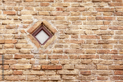 Brick wall with a small square window. Brown brick wall of a house in the old town with a rhombus window