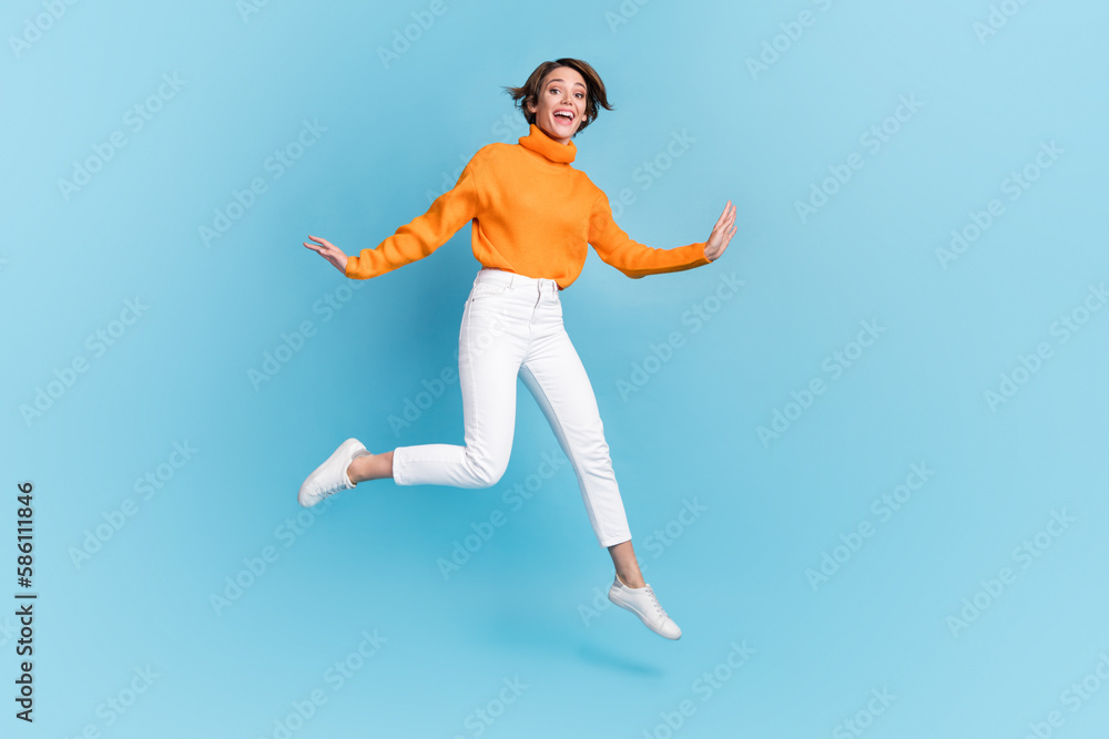 Full size photo of pretty young girl jumping excited cheerful energetic dressed stylish orange clothes isolated on blue color background