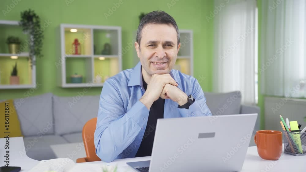 Home office worker man looking at camera and smiling.
Man doing his job in home office looks at camera and smiles.

