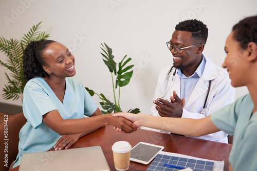 Bilde på lerret Two doctors shake hands while colleague claps, medical promotion achievement