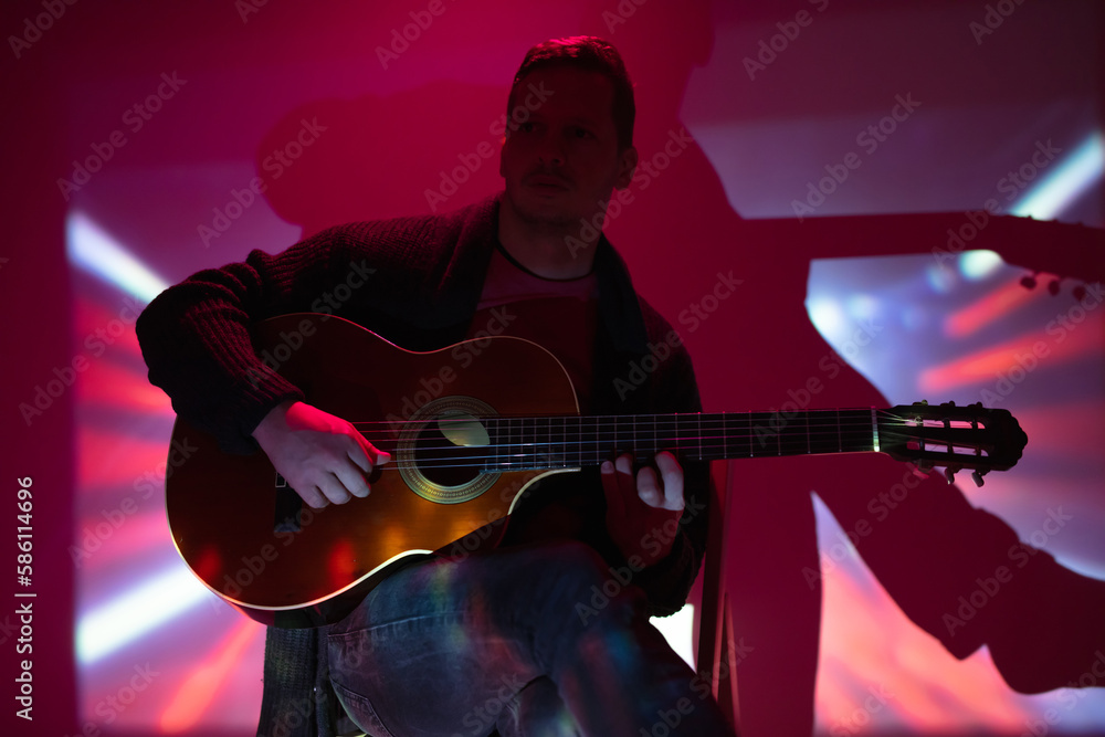 Obraz premium Musician playing acoustic guitar in a foggy club with colorful lights.