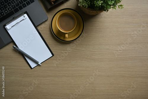 Blank clipboard, cup of coffee and laptop computer on wooden office desk. Top view with copy space