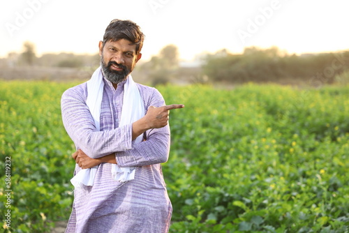 Happy rural Indian a farmer pointing at his right side while looking at the camera.