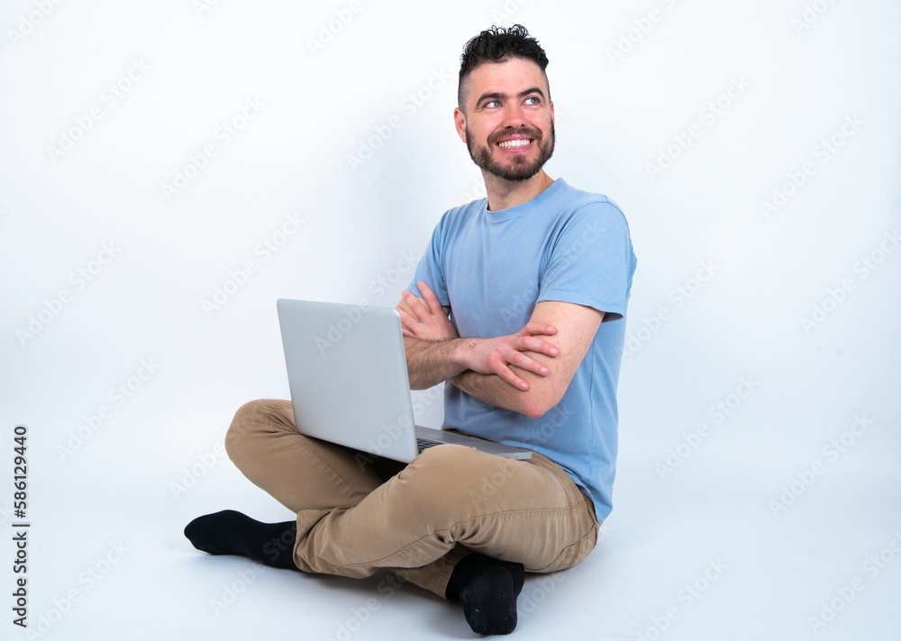 Dreamy rest relaxed Young caucasian man with laptop sitting over white studio crossing arms, looks good copyspace