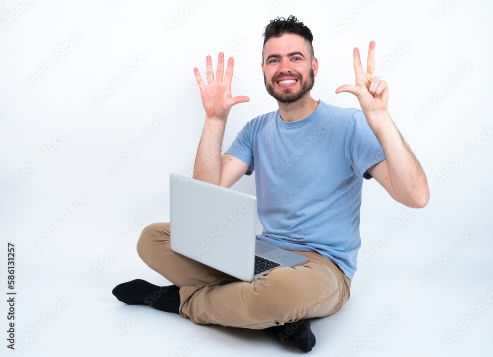 Young caucasian man with laptop sitting over white studio showing and pointing up with fingers number eight while smiling confident and happy. Young caucasian man with laptop sitting over white studio showing and pointing up with fingers number eight while smiling confident and happy.