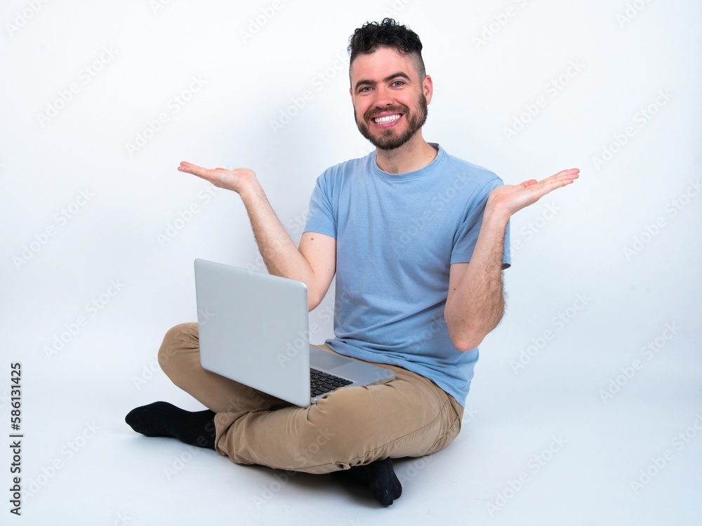 Cheerful cheery optimistic Young caucasian man with laptop sitting over white studio holding two palms copy space Cheerful cheery optimistic Young caucasian man with laptop sitting over white studio holding two palms copy space