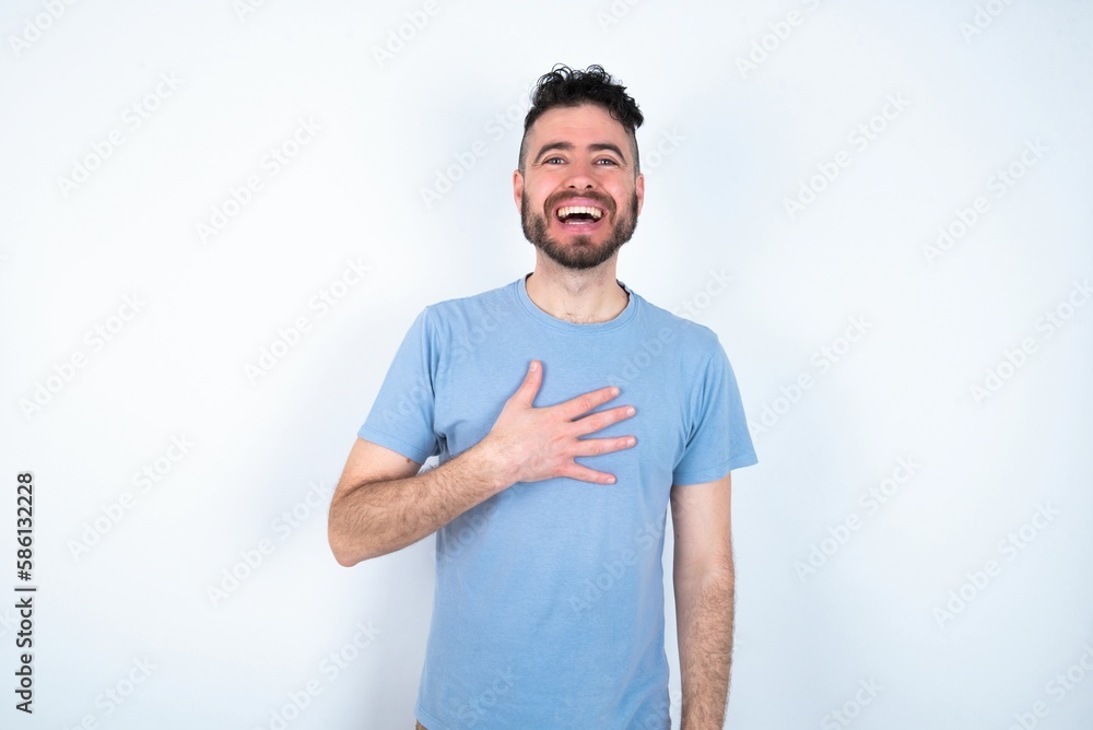 Fototapeta premium Young caucasian man wearing blue T-shirt over white background smiles toothily cannot believe eyes expresses good emotions and surprisement