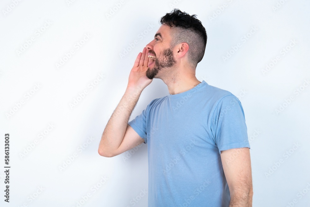 Young caucasian man wearing blue T-shirt over white background look empty space holding hand face and screaming or calling someone. Young caucasian man wearing blue T-shirt over white background look empty space holding hand face and screaming or calling someone.