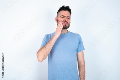 Young caucasian man wearing blue T-shirt over white background with toothache