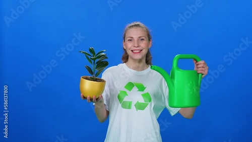 Ecology, pretty woman ecoactivist looks into the camera, holding a watering can and plant in his hands on a blue background, template, greening the planet. photo