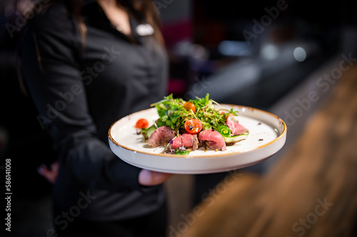 Waiter holds a plate with meat salad in the restaurant