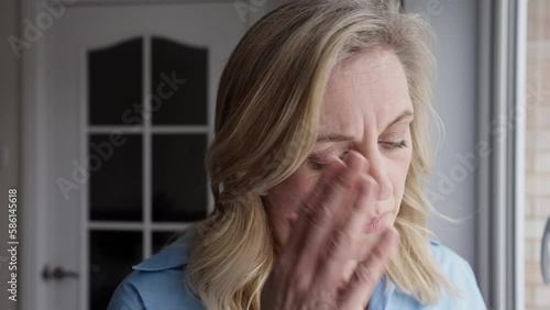 Menopausal Mature Woman At Home Standing By Window Suffering With Headache Or Migraine Pain