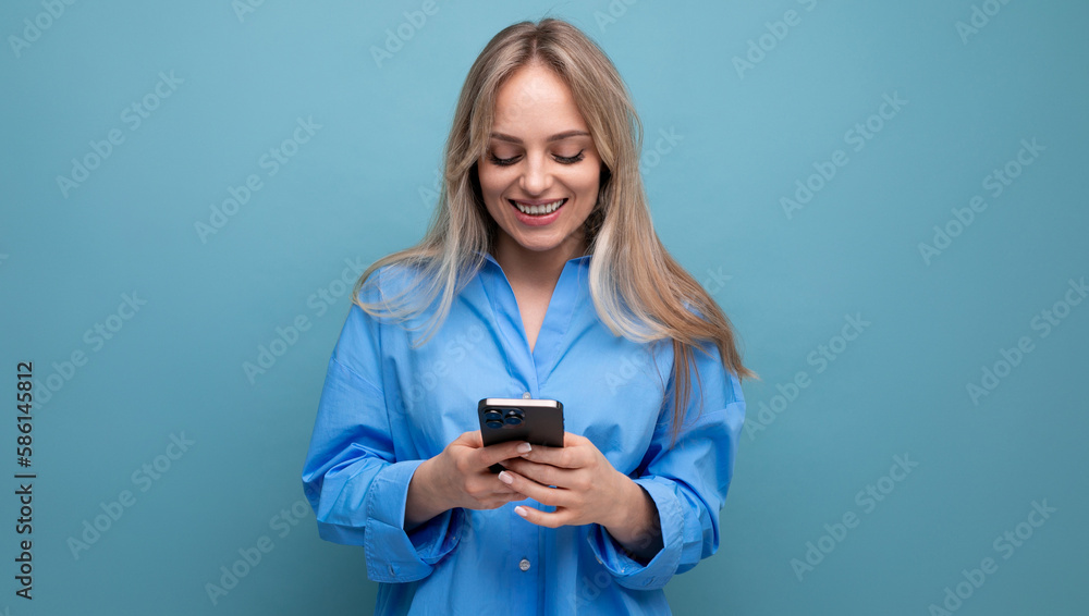 joyful charming blonde woman chatting in a smartphone application on a blue bright background joyful charming blonde woman chatting in a smartphone application on a blue bright background