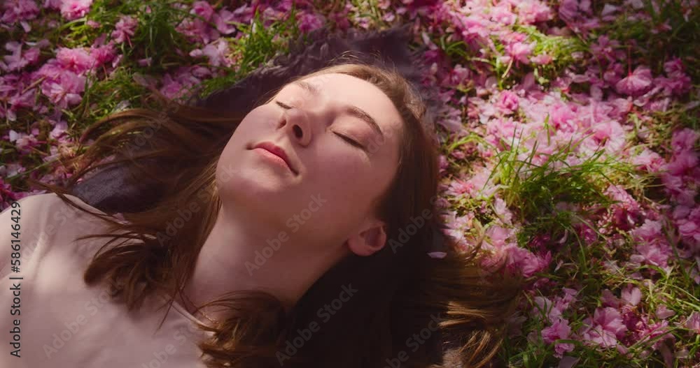 Young brunette lying on fallen cherry blossom tree leaves, close up view Young brunette lying on fallen cherry blossom tree leaves, close up view