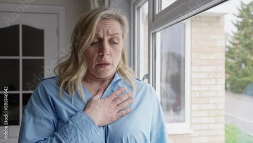 Menopausal Mature Woman At Home Standing By Window Suffering With Heart Palpitations