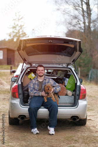 A young male hugging his dog while sitting on the backside of the car before moving to their next house. A happy young man with his puppy. photo