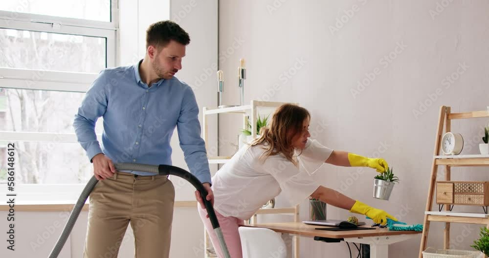 Couple Vacuuming Hardwood Floor And Dusting Desk Couple Vacuuming Hardwood Floor And Dusting Desk
