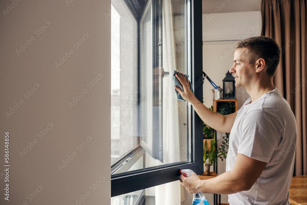 A happy man is cleaning window at his apartment.