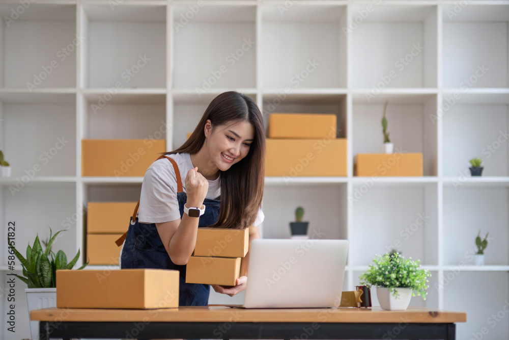 Happy young Asian woman entrepreneur, Smile for sales success after checking order from online shopping store in a smartphone at home office, Concept of merchant business online and eCommerce Happy young Asian woman entrepreneur, Smile for sales success after checking order from online shopping store in a smartphone at home office, Concept of merchant business online and eCommerce