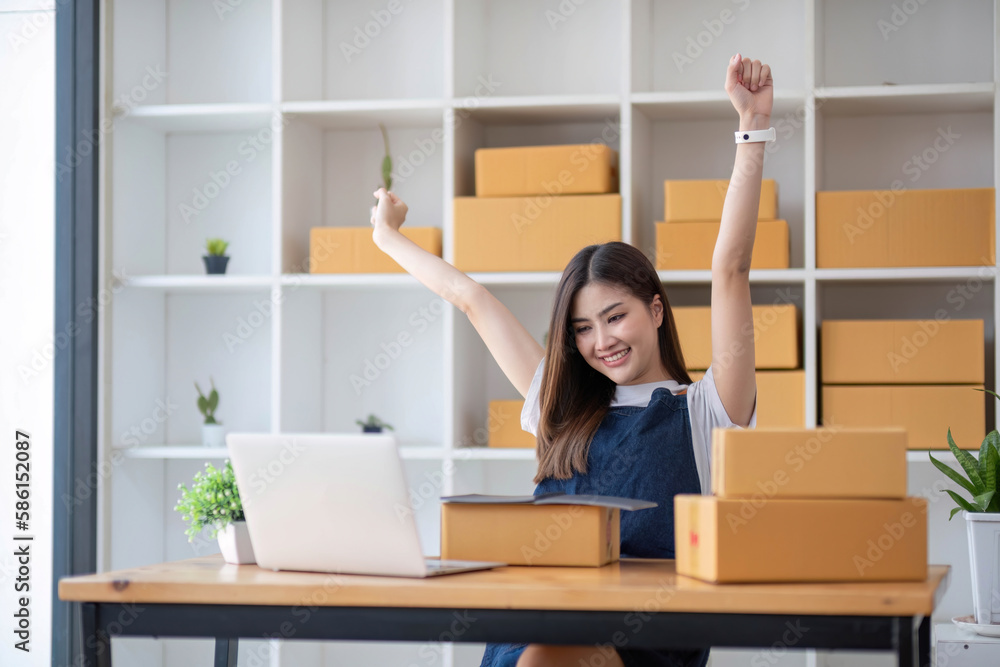 Happy young Asian woman entrepreneur, Smile for sales success after checking order from online shopping store in a smartphone at home office, Concept of merchant business online and eCommerce Happy young Asian woman entrepreneur, Smile for sales success after checking order from online shopping store in a smartphone at home office, Concept of merchant business online and eCommerce