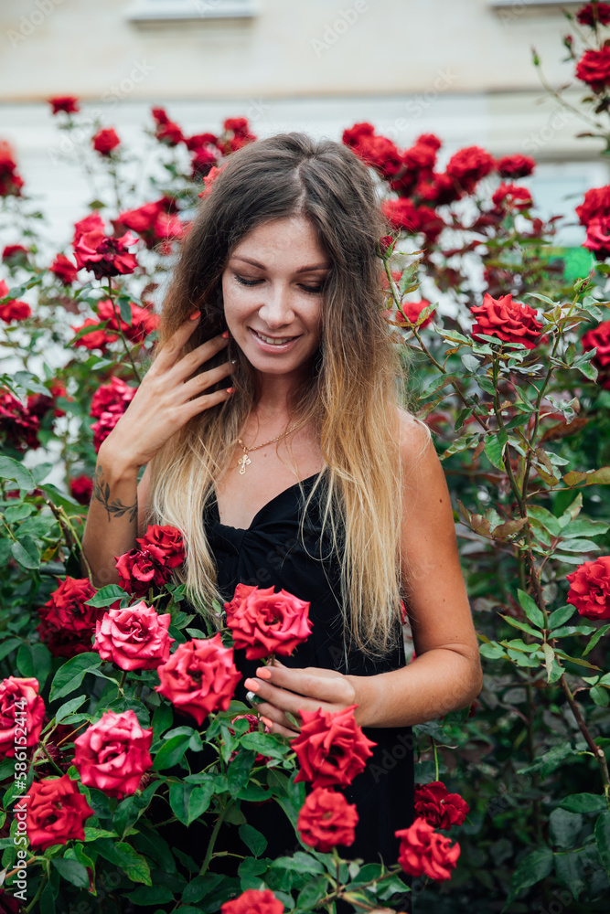 a woman stands in the rose bushes in the park on the street walk a woman stands in the rose bushes in the park on the street walk