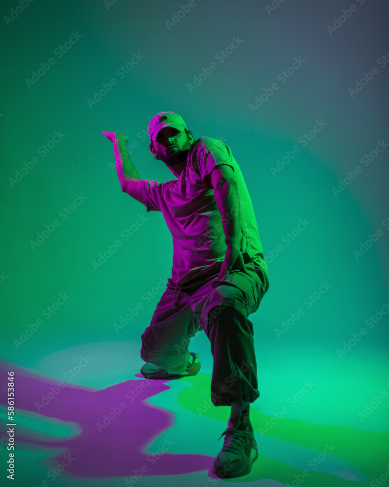 Professional male dancer in fashionable clothes dancing in a creative studio with cyan and magenta light