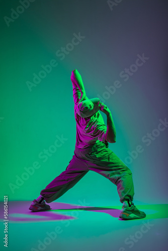 Stylish professional dancer man with a cap in trendy fashion clothes dancing in a colorful creative studio with cyan and pink lights