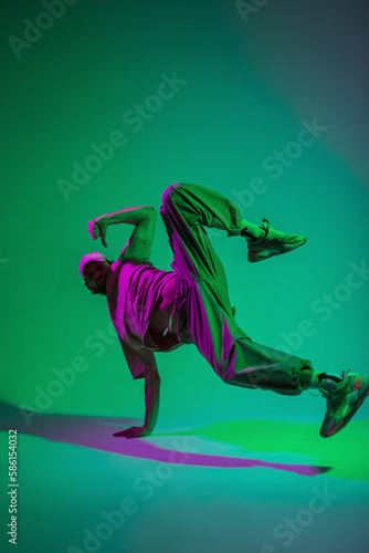 Stylish professional dancer guy hip hop b-boy in fashionable clothes with a cap and sneakers dances on hand in a creative studio with magenta and cyan color © alones