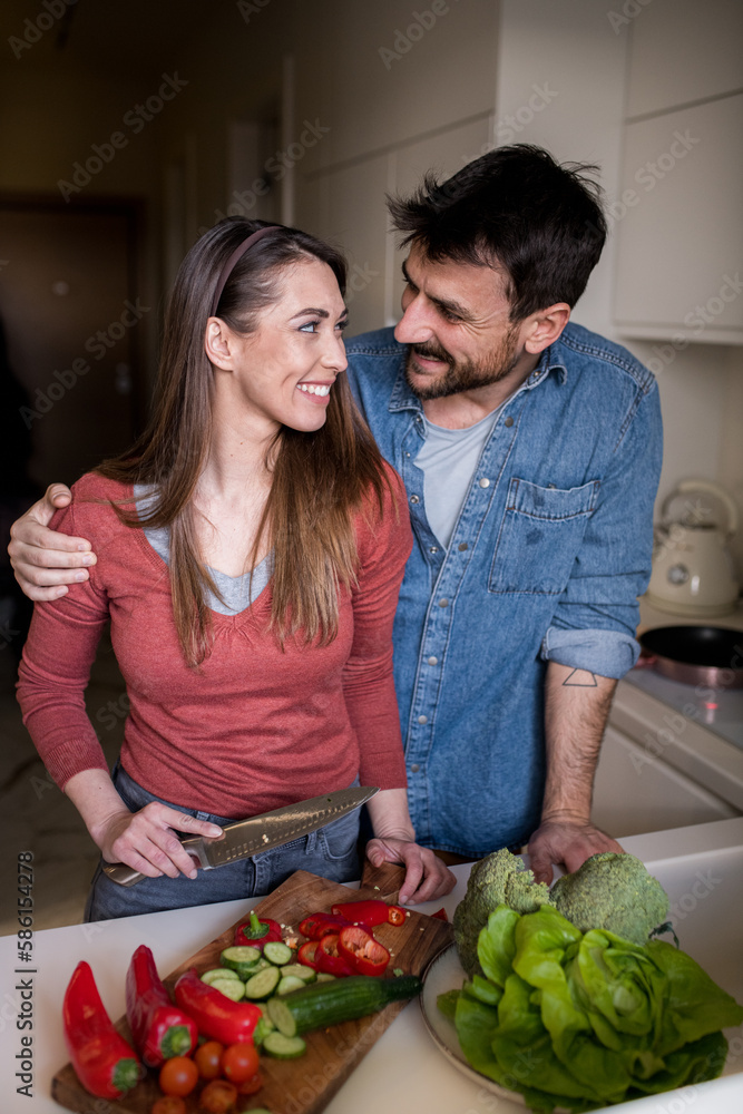 Lovely young couple looking at each other lovingly while making a meal together. Lovely young couple looking at each other lovingly while making a meal together.