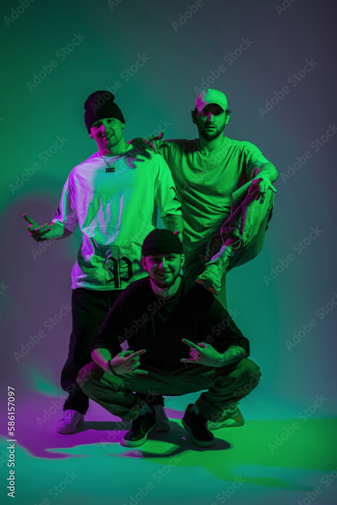 Funny cool stylish handsome guys friends team in fashion clothes posing together in creative color studio with green and pink light