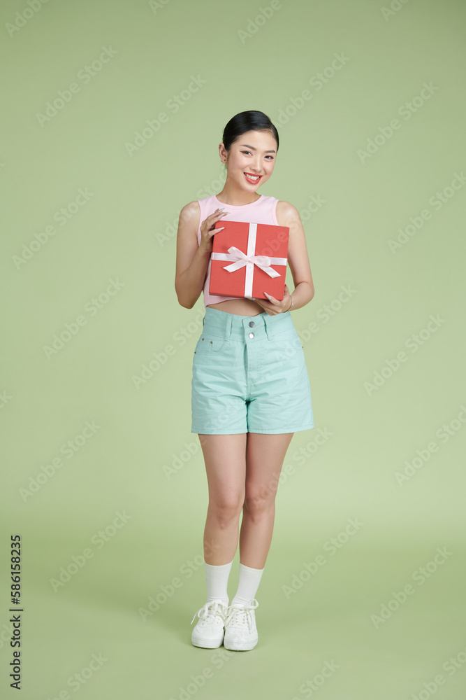 Happy woman holding gift box and looking at the camera while enjoys over green background Happy woman holding gift box and looking at the camera while enjoys over green background