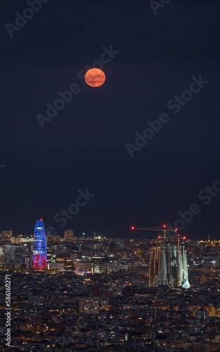 Photography Night panoramic view of the city of Barcelona and the Sagrada Familia illuminated, with the full moon in the sky, over the sea