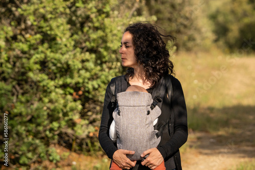 Tableau sur toile Young mom walking while carrying her newborn baby in an ergonomic carrier backpack