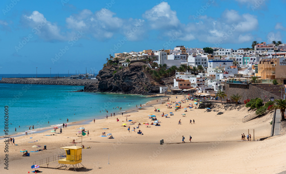 Vista panorámica de la playa de Morro Jable con arena blanca y mar turquesa llena de gente disfrutando del sol con el pueblo al fondo la arquitectura tradicional Fuerteventura Islas Canarias