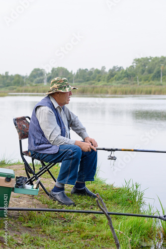 Happy positive cheerful old man enjoying fish, hold a fishing rod, sit on a chair. Leisure and outdoor hobbies