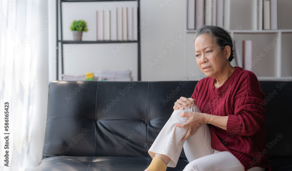 Asian elderly woman sitting with knee pain on sofa at home. Asian elderly woman sitting with knee pain on sofa at home.