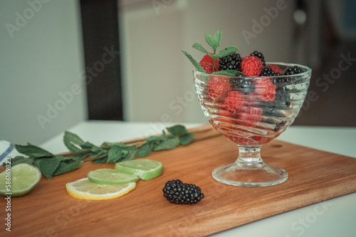 A bowl of fruit on a cutting board with a lime and blackberries. photo