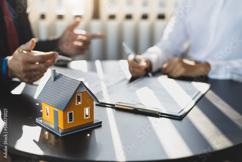 Businessman in suit in his office showing home insurance policy and pointing with a pen where the policyholder must to sign. Insurance agent consulting real estate insurance detail to customer.