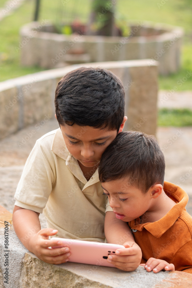 Vertical photo of special needs child and sibling engrossed in phone in natural setting Vertical photo of special needs child and sibling engrossed in phone in natural setting