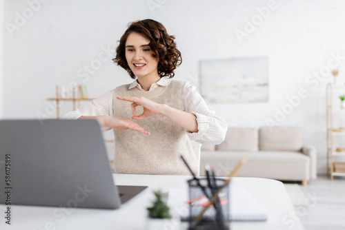 happy teacher with curly hair showing sign language gesture during online lesson on laptop. photo