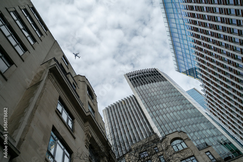 View to London skyscrapers and flying plane from below at cloudy spring day