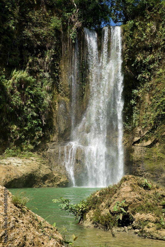 Obraz premium The idyllic Camugao Waterfall in Siquijor in the Philippines that flow into a natural pool of water surrounded by the light-lit rainforest.