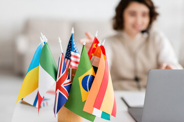 selective focus of various international flags near blurred laptop and language teacher having online lesson at home.