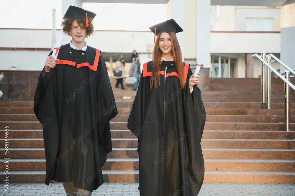 Happy friends on graduation day. Portrait of two cheerful joyful students standing near university building.