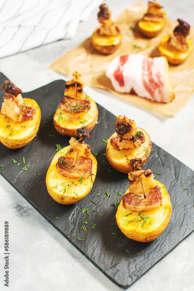 Golden potato halves baked with bacon served on a black board.